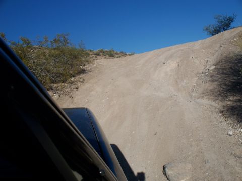 1996 Ford Bronco - A dark SUV navigates a steep dirt road under a clear blue sky in a desert landscape.