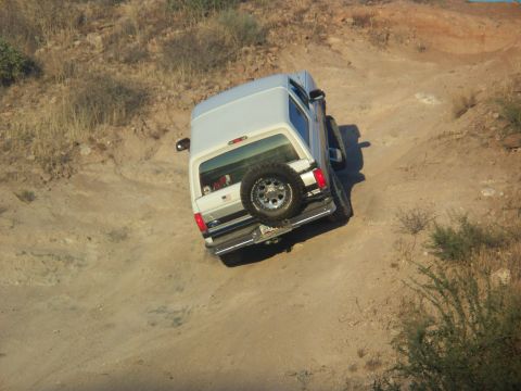 1996 Ford Bronco - A white 1996 Ford Bronco navigates a dusty off-road trail from a rear perspective.