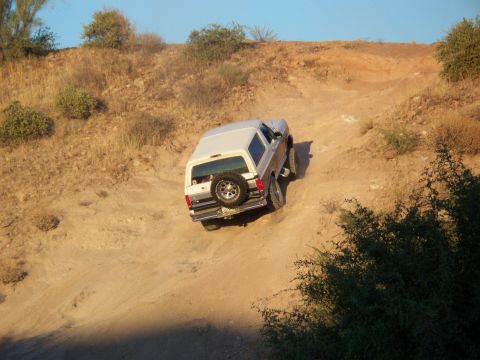 1996 Ford Bronco - Ford Bronco navigates a steep, off-road dirt trail under a clear blue sky.