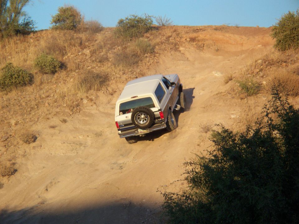 1996 Ford Bronco driving up a sandy, dry hill with sparse vegetation