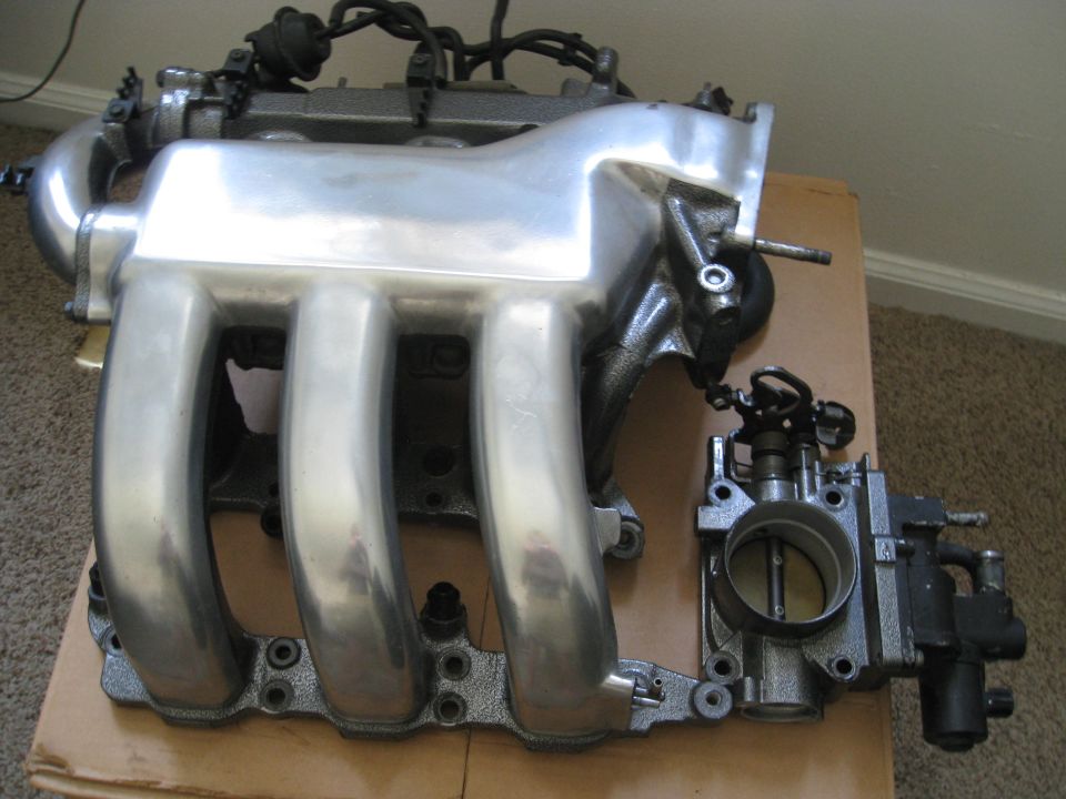 Polished aluminum intake manifold and black throttle body on a cardboard surface
