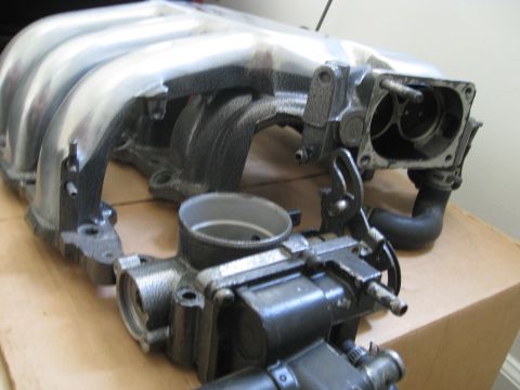 1994 Ford Probe - This photo shows a disassembled engine part, specifically an intake manifold and throttle body, on a cardboard surface.