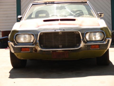 1973 Ford Ranchero - This vehicle's front end features a wide grille and distinctive dual headlights, with a weathered appearance.