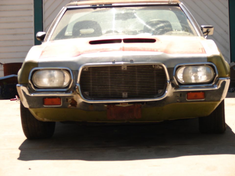 Front view of green 1970s Ford in primer with hood scoop, sanded hood and chrome bumper