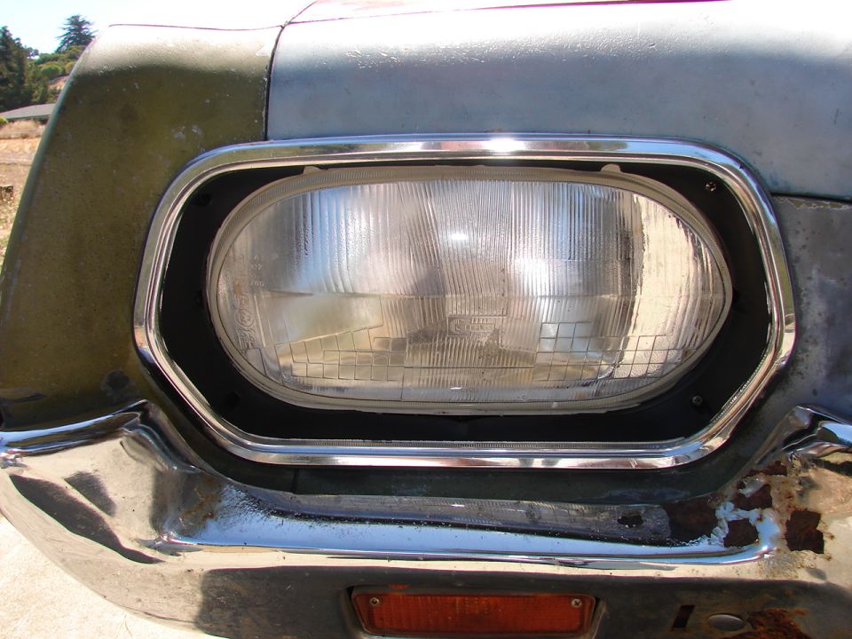 Headlight and chrome bumper on a weathered vehicle, showing rust and damage