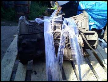 1989 Ford Bronco - This is a transmission, likely for a vehicle, covered in plastic and resting on wooden planks.