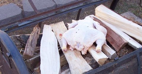 1990 Ford Bronco - A whole raw chicken is placed on wooden planks inside a metal fire pit with firewood.