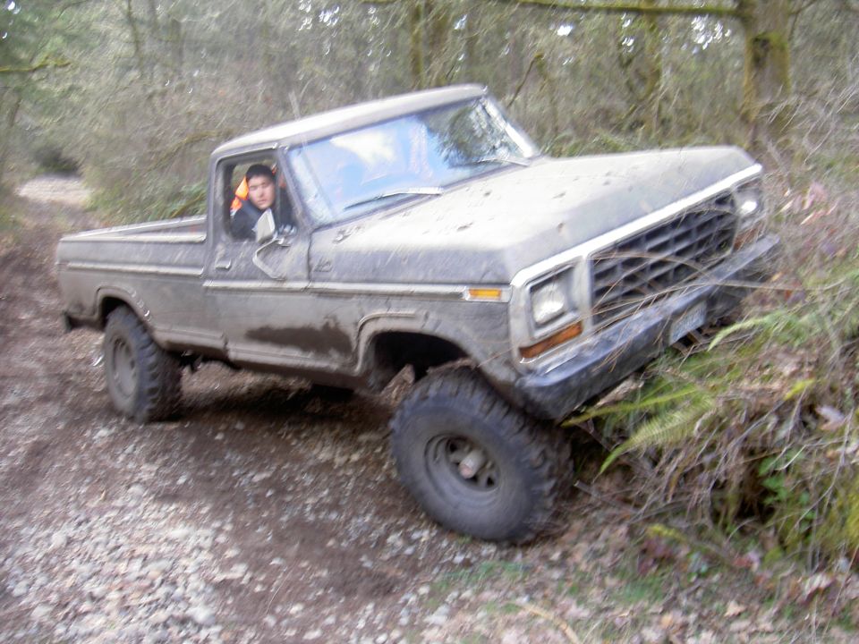 Muddy lifted Ford F-150 pickup flexing on a forest trail with front wheel off the ground