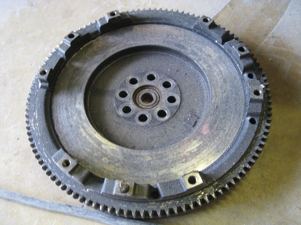 Close-up of a dusty automotive flywheel with a toothed outer edge and bolt holes