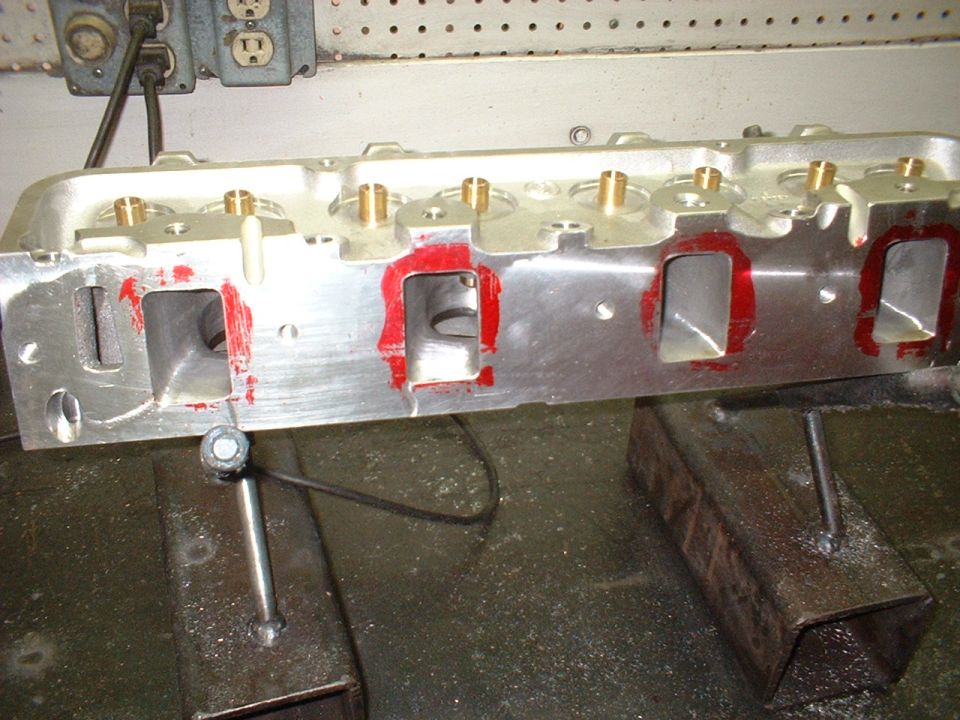 Aluminum engine cylinder head with red sealant around ports, mounted on a workbench