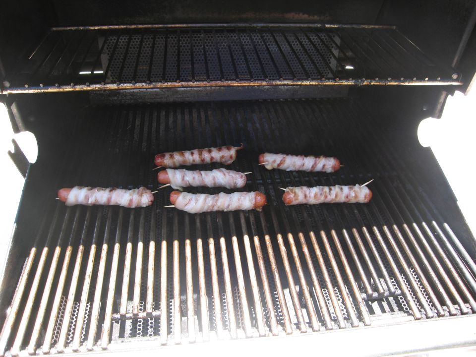 Hot dogs wrapped in bacon on a grill with a Supermotors.net logo