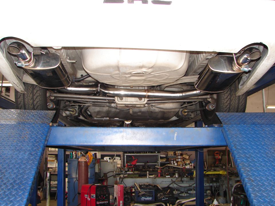 Underside of a car showing a dual-tip aftermarket exhaust system and fuel tank