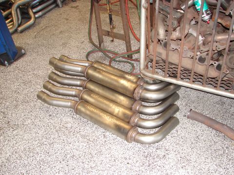 1992 Ford Taurus - Several Magnaflow exhaust mufflers are stacked on a shop floor next to other exhaust components.