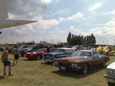 1991 Ford Crown Victoria - A brown coupe from the 1970s is parked on a grassy field with other vintage vehicles under a cloudy sky.