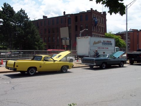 1975 Ford Ranchero - Two Ford Rancheros are parked on a street with their hoods open, with a brick building and a box truck behind them.