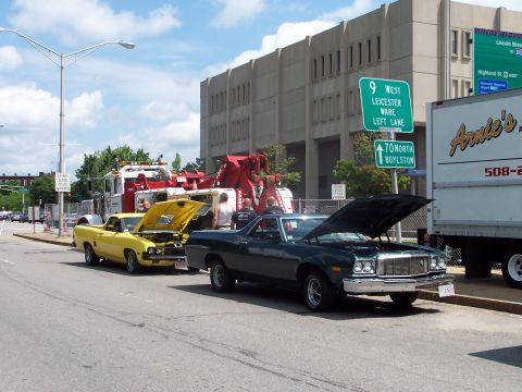 1975 Ford Ranchero - Two Ford Rancheros are parked on a street with their hoods up, alongside tow trucks and a delivery truck.