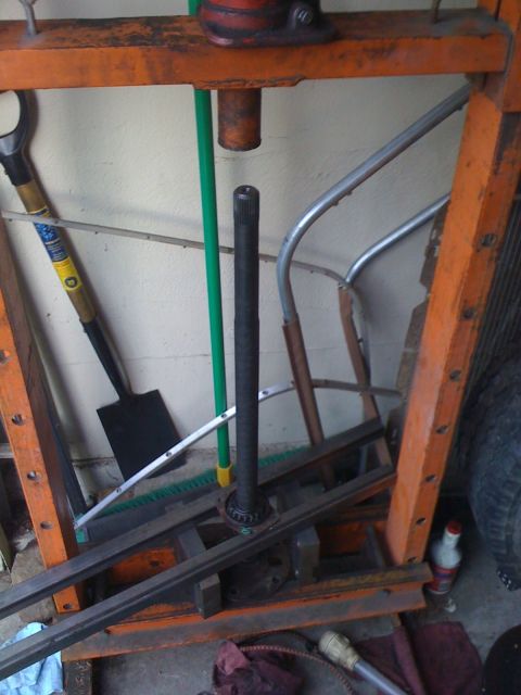 1989 Ford Bronco - Axle shaft and bearing assembly on a press, with tools in the background.