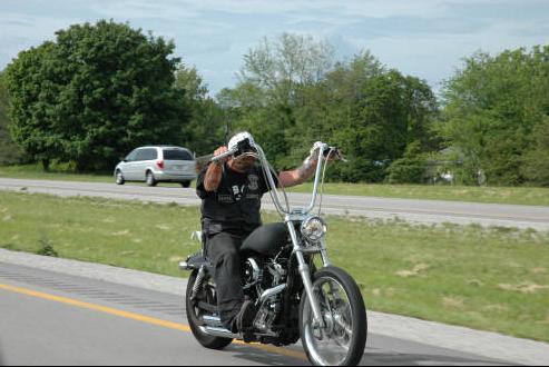 Rider in patched leather vest on black ape-hanger chopper riding a rural highway