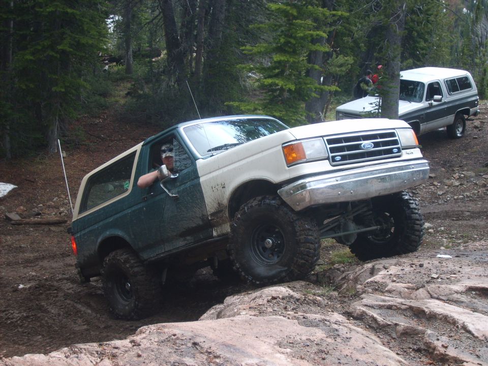 Green and white Ford Bronco climbing rocks on a trail, another SUV behind it