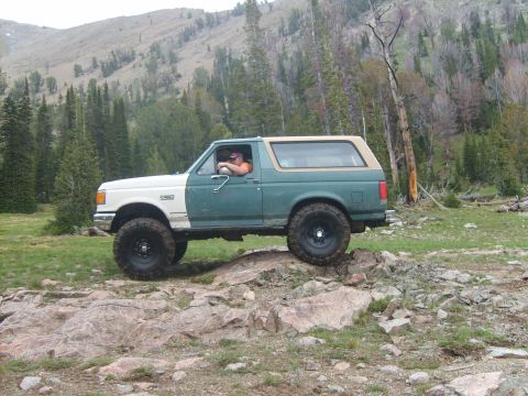 1989 Ford Bronco - A two-tone green and white 1989 Ford Bronco navigates a rocky trail in a mountainous, wooded area.