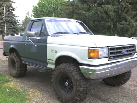 1989 Ford Bronco - This lifted pickup truck has a dark green body and a white front end, with large off-road tires.
