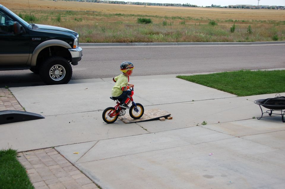 Dark green Ford Super Duty pickup at a curb, child on a red bike on the driveway