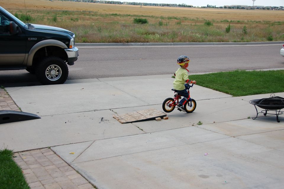 Child in a helmet riding a small red bicycle on a driveway near a parked green Ford F-250