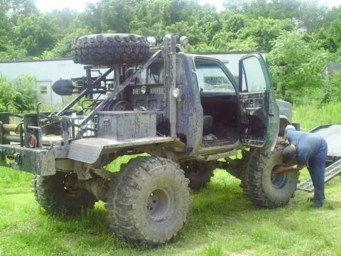 1990 Ford Bronco - A heavily modified pickup truck, possibly a tow rig, is shown with its doors open and a person working on a tire. The text "DIRTY HOOKER" i…
