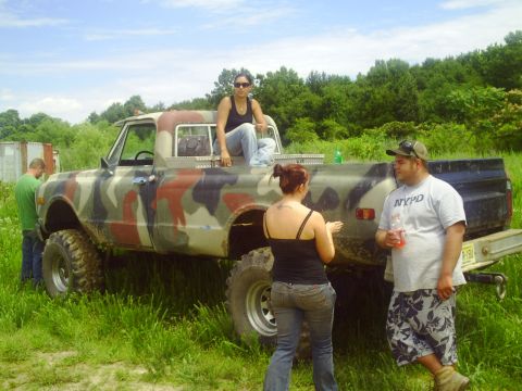 1990 Ford Bronco - People gather around a lifted, camouflaged pickup truck in a grassy, outdoor setting.
