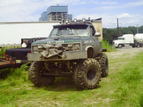 1990 Ford Bronco - A heavily modified pickup truck sits in a grassy area with industrial buildings in the background.