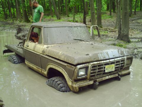 1990 Ford Bronco - This 1979 Ford F-Series pickup truck is deeply stuck in mud, with two people inside and another person observing.