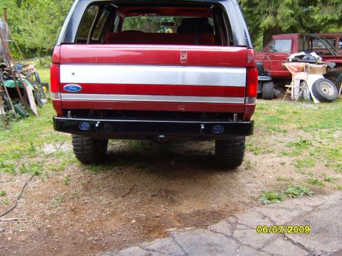 1989 Ford Bronco - The rear of a red Ford Bronco is shown with a custom black bumper and a Ford emblem on the tailgate.