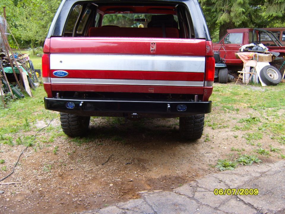 Rear view of red Ford Bronco with aftermarket bumper. Another red truck is parked behind it