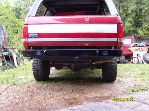 1989 Ford Bronco - Rear view of a red 1987 Ford Bronco with a custom bumper and large tires, parked outdoors.