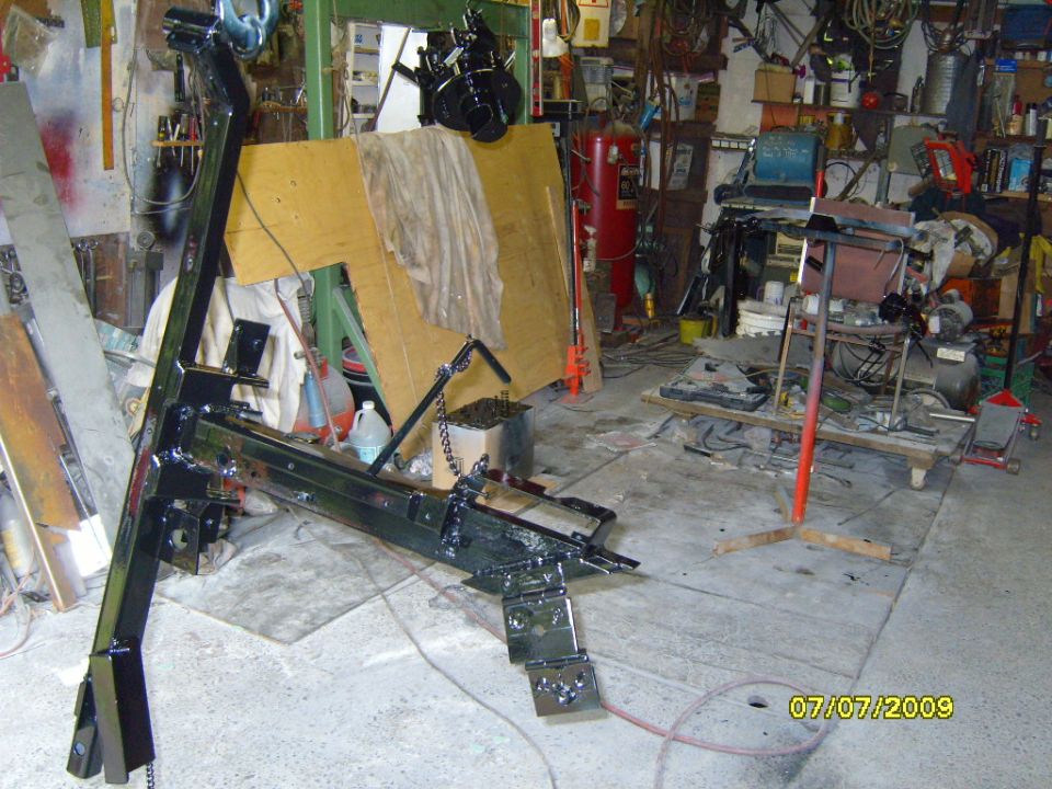 Black metal frame with chains and brackets, likely a lift or jack, in a cluttered garage