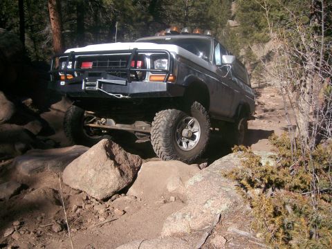 1978 Ford Bronco - A 1978 Ford Bronco navigates a challenging rocky path in a wooded area.