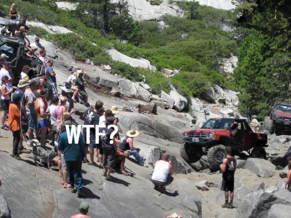 Red off-road pickup truck on rocks, spectators watching