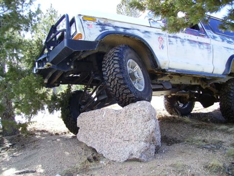 1978 Ford Bronco - A white 1978 Ford Bronco navigates an off-road obstacle, with its front tire on a large rock.