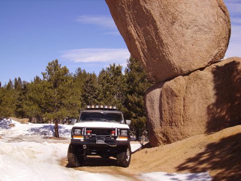 1978 Ford Bronco - A white 1978 Ford Bronco is parked on a snowy dirt road next to a massive rock formation.