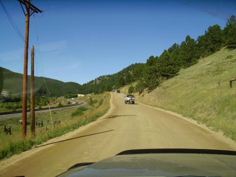 1978 Ford Bronco - Driving on a dusty road through a rural, mountainous area with trees and train tracks visible.