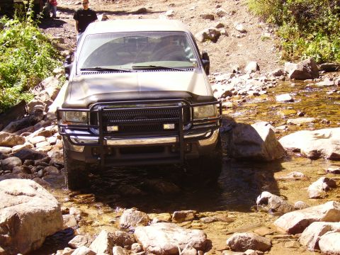 1978 Ford Bronco - A Ford F-Series truck navigates a rocky stream, with people visible on the bank above.