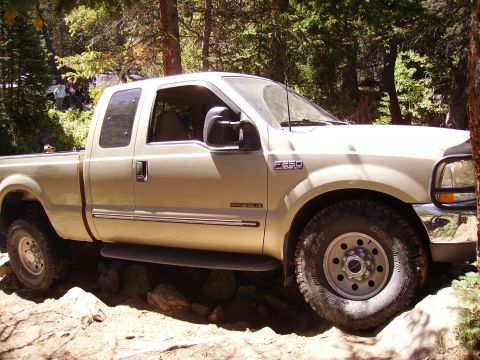 1978 Ford Bronco - A tan Ford F-250 Super Duty pickup truck navigates a rocky off-road trail in a wooded area.