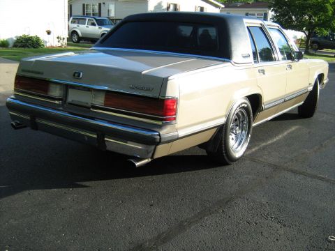 1988 Mercury Grand Marquis - The rear of a 1988 Mercury Grand Marquis is shown parked on an asphalt surface with a house and another vehicle in the background.