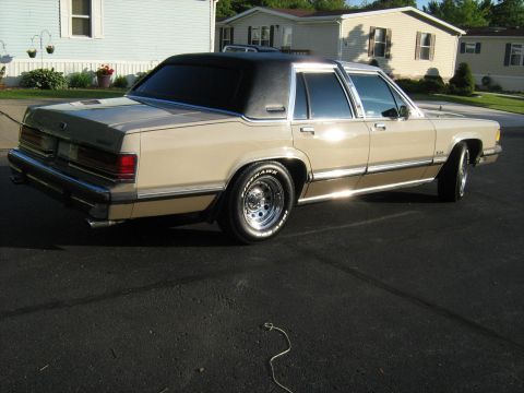 1988 Mercury Grand Marquis - A tan 1988 Mercury Grand Marquis sedan with a black vinyl roof is parked on asphalt.
