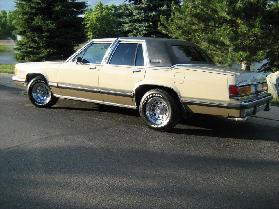 Tan Mercury Grand Marquis sedan 3/4 rear view with black vinyl roof, chrome wheels