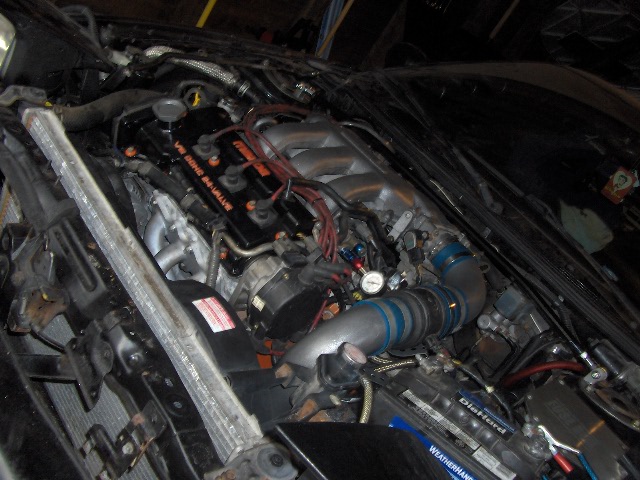 Engine bay with V6 DOHC 24-VALVE engine cover, custom piping, and a gauge