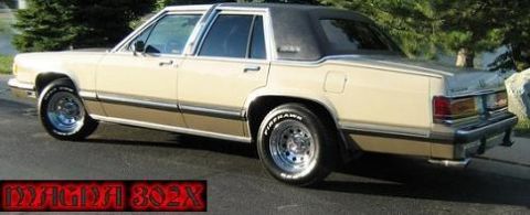1988 Mercury Grand Marquis - A tan 1988 Mercury Grand Marquis sedan is parked outdoors on a paved surface with trees in the background.