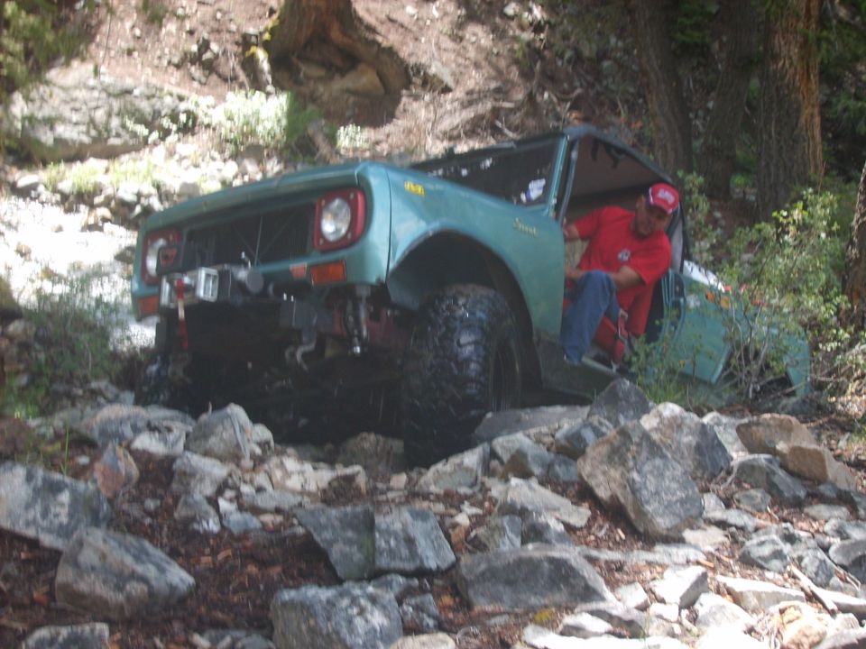 Green off-road vehicle navigating rocky terrain, driver in red shirt visible