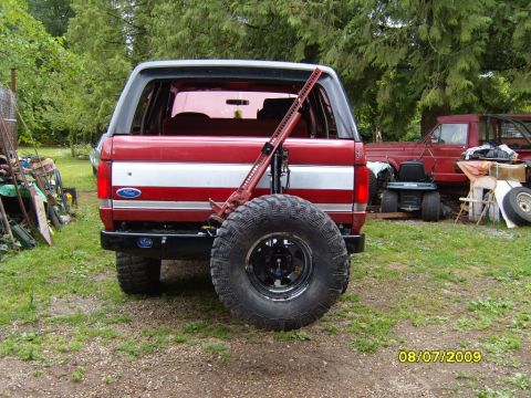 1989 Ford Bronco - Rear view of a red and white Ford Bronco with a spare tire and a Hi-Lift jack attached to the tailgate.