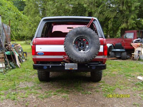 1989 Ford Bronco - Rear view of a red and white 1989 Ford Bronco, an external spare tire and a prominent white stripe.